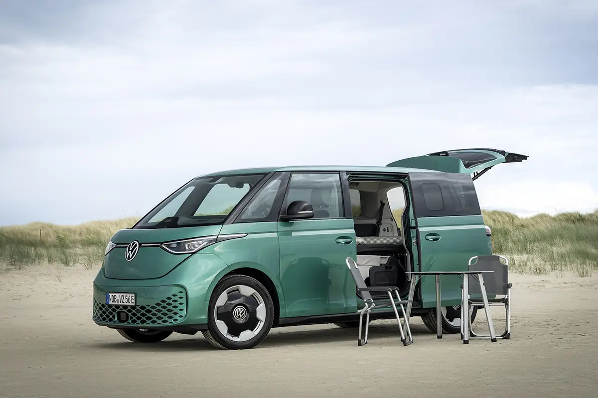 Ein minzgrüner VW ID. Buzz steht mit geöffneter Heckklappe und offener Schiebetür in einer Dünenlandschaft als kompakter Weekender.