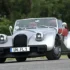 Frontansicht des silbernen Morgan Supersport Roadsters mit geöffnetem Verdeck und rotem Interieur auf einer Landstraße.