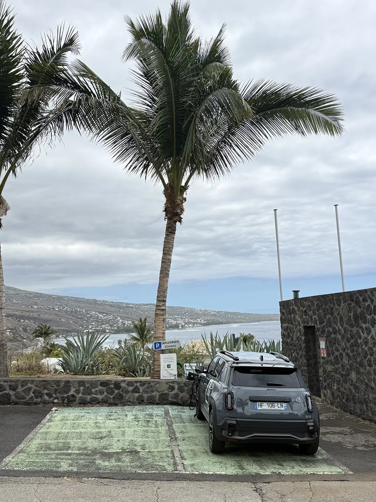Ein grauer Renault 4 Elektro steht unter einer Betonbrücke auf einem orange markierten Parkplatz mit der Aufschrift RUN CHARGE und ist an einer modernen Ladesäule angeschlossen.
