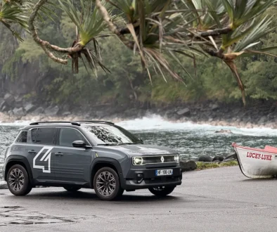 Ein grauer Renault 4 Elektro mit einer markanten weissen Startnummer 4 auf der Vordertür parkt an einer Küstenstrasse auf La Réunion im Hintergrund eines weissen Bootes mit der Aufschrift LUCKY LUKE.