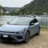 Schrägansicht von vorne auf das blaugraue Elektro-Kompakt-SUV Leapmotor B05, das auf kieseligem Untergrund am Ufer einer Flusslandschaft vor bewaldeten Hügeln steht.