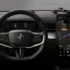 Blick auf das minimalistische, schwarze Cockpit eines Polestar-Elektrofahrzeugs mit digitalem Kombiinstrument hinter dem Dreispeichen-Lenkrad und einem großen, vertikalen Infotainment-Touchscreen, der eine aktive Navigationskarte anzeigt.