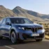 Ein moderner, tiefblauer BMW iX3 Elektro-Crossover aus der zukunftsweisenden „Neuen Klasse“ in dynamischer Fahrt auf einer asphaltierten Landstraße vor einer weitläufigen, trockenen Wüsten- und Bergkulisse.