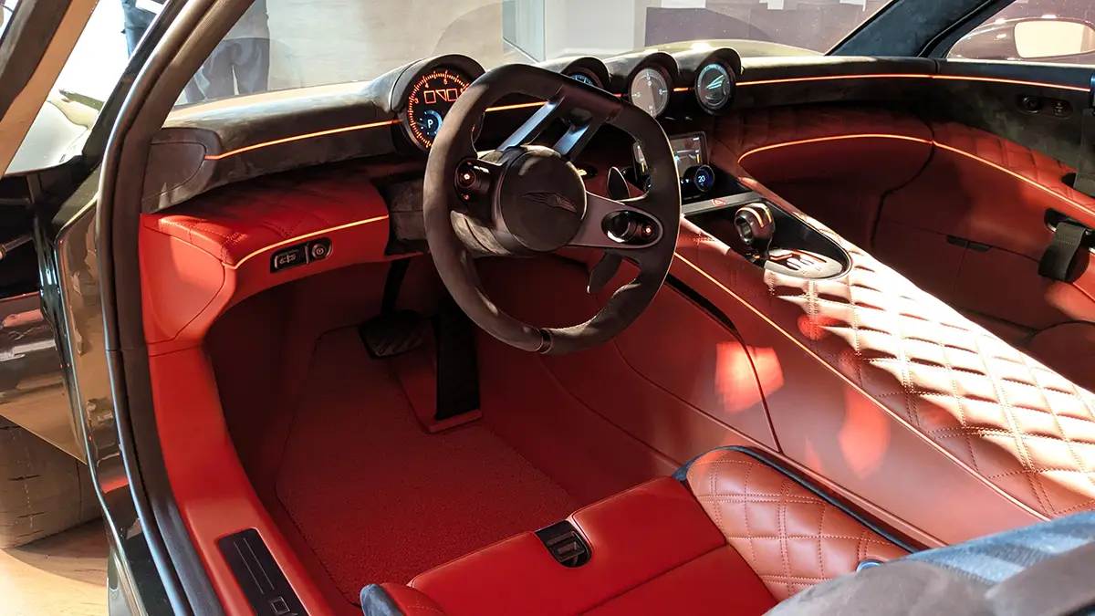 Detailansicht des fahrerorientierten Twin-Cockpits im Genesis Magma GT mit Sportlenkrad, haptischen Bedienelementen und einem zentralen analogen Drehzahlmesser.