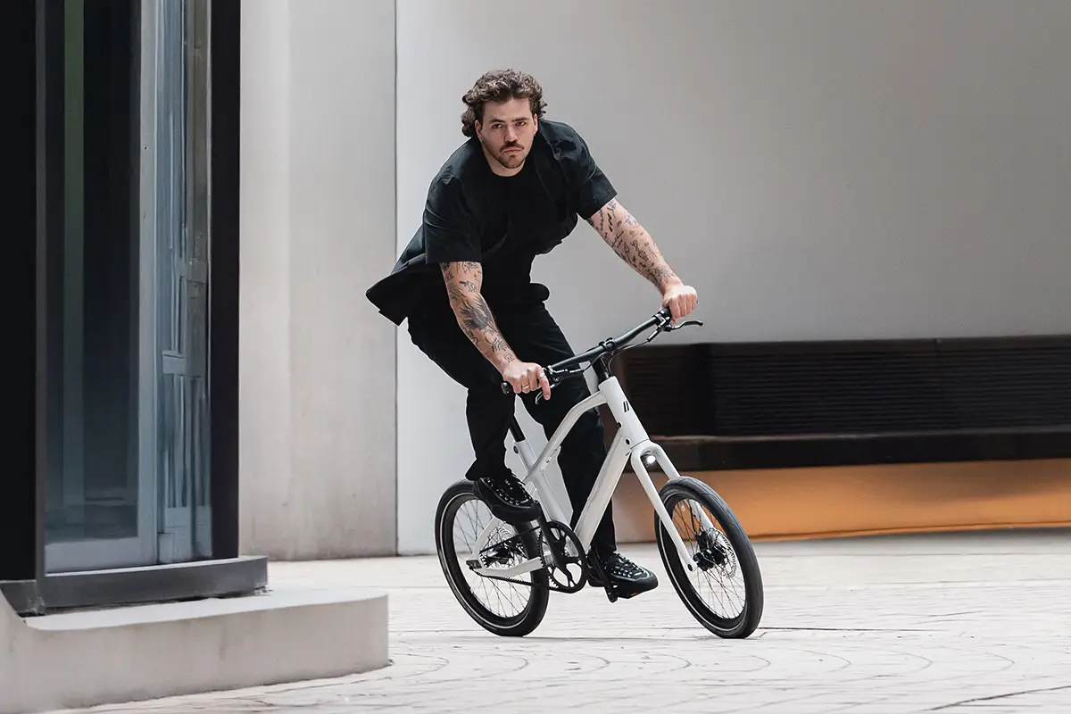 Ein Mann im schwarzen Outfit fährt sportlich mit dem weißen 20-Zoll-Kompaktrad Schindelhauer Neo über eine Betonstufe im urbanen Raum.