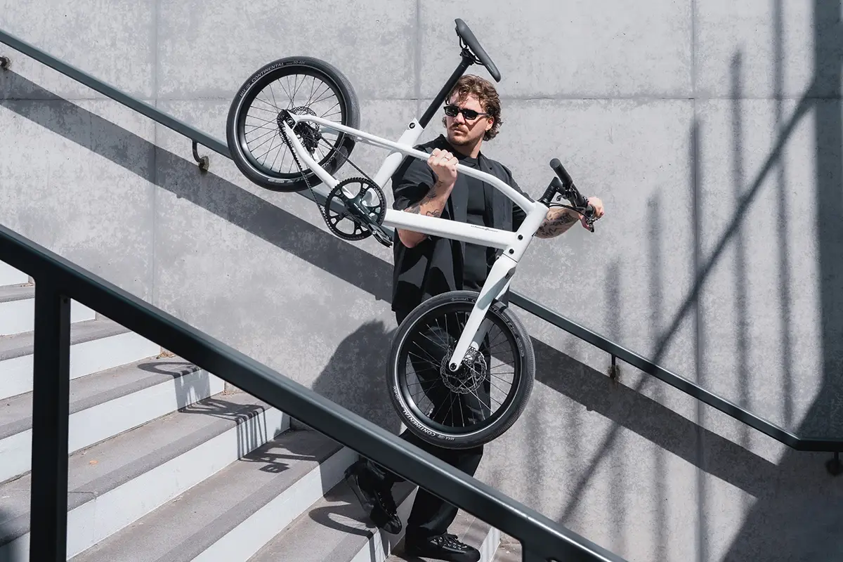 Ein Mann trägt das extrem leichte, weiße Schindelhauer Neo Singlespeed-Fahrrad mühelos an einer Hand eine urbane Betontreppe hinauf.
