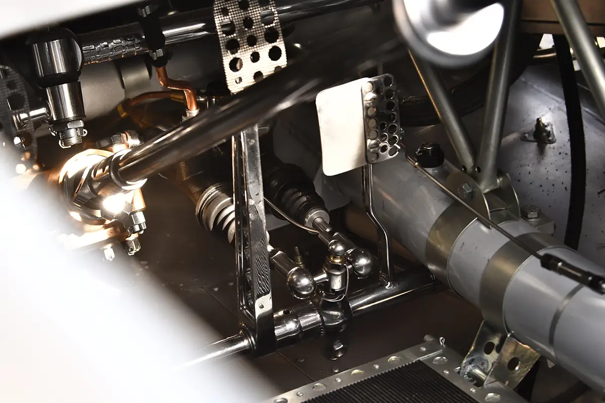 Detailansicht des engen mechanischen Fussraums im Auto Union Rekordwagen mit gelochten Metallpedalen und der freiliegenden, verchromten Lenkstange.