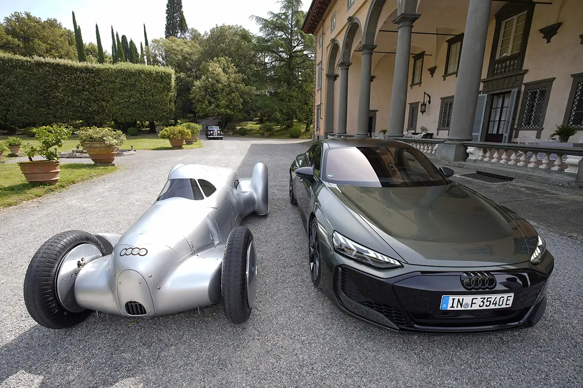 Der historische Stromlinienwagen und der moderne Audi e-tron GT stehen nebeneinander in der gepflasterten Auffahrt einer prachtvollen, historischen toskanischen Villa.
