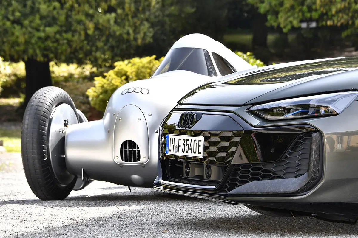 Makroaufnahme der abgerundeten, silbernen Frontpartie des historischen Auto Union Typ A direkt neben der modernen, wabenförmig gemusterten Kühlergrill-Maske des Audi RS e-tron GT performance.