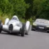 Der historische, silberne Auto Union Typ A Stromlinienwagen „Lucca“ fährt auf einer schmalen Asphaltstrasse in der Toskana, dicht gefolgt von einem modernen, dunkelgrauen Audi RS e-tron GT.