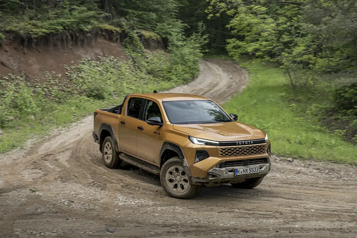 Der neue Toyota Hilux Pickup in Gold-Bronze meistert eine unbefestigte, schlammige Offroad-Piste im Wald.