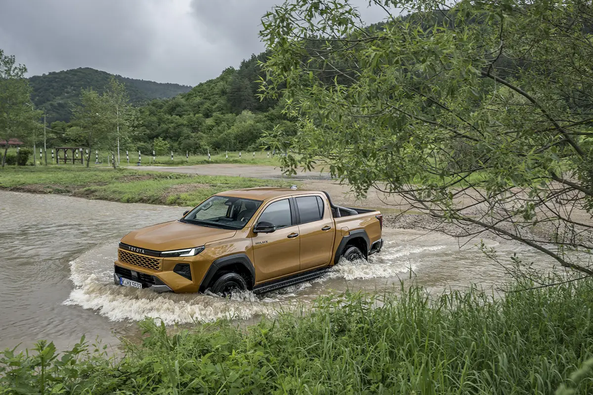 Heckperspektive des Toyota Hilux Allrad-Pickups beim Erklimmen eines steilen, rutschigen Schlammhügels im Wald.