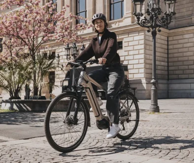 Eine E-Bikerin fährt im urbanen Raum auf einem Pflastersteinweg vor einem historischen Steingebäude in Hamburg mit einem City-E-Bike, das mit dem neuen Bosch Active Line Plus Smart System ausgestattet ist.