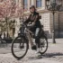 Eine E-Bikerin fährt im urbanen Raum auf einem Pflastersteinweg vor einem historischen Steingebäude in Hamburg mit einem City-E-Bike, das mit dem neuen Bosch Active Line Plus Smart System ausgestattet ist.