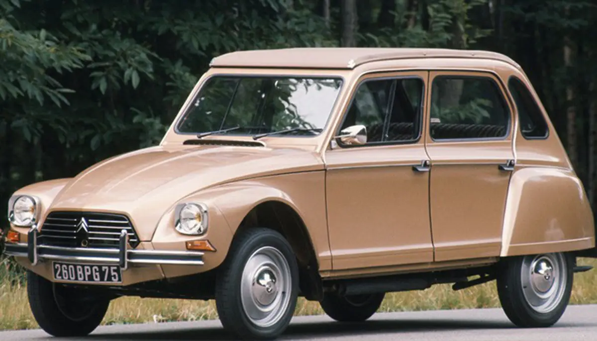 Classic beige vintage car parked on a road with greenery in the background, side profile view.