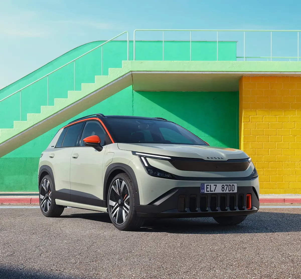 Der helle Skoda Epiq Elektro-Crossover parkiert vor einer bunten, gelb-grünen Fassade mit Freitreppe.