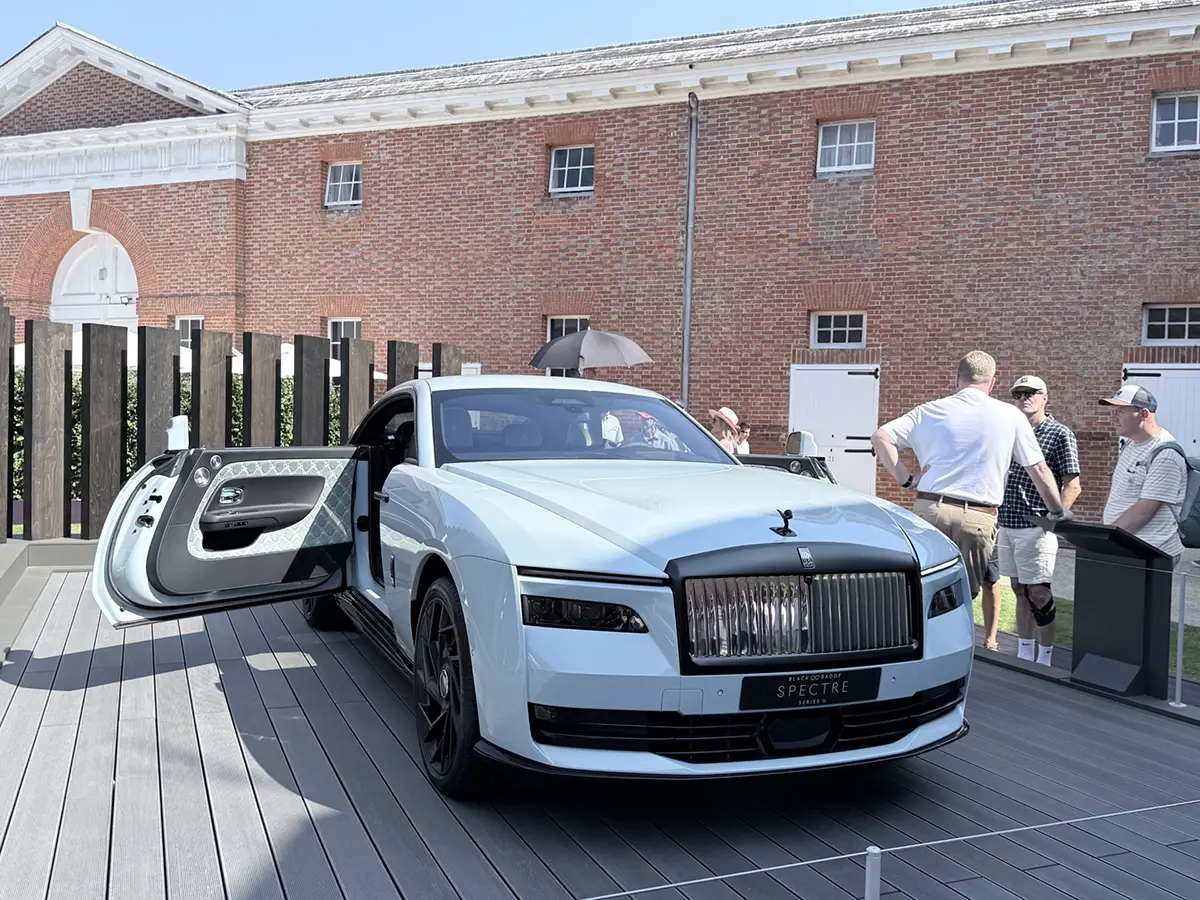 Ein luxuriöses, hellgraues Rolls-Royce Coupé mit geöffneter Coach-Door steht auf einer Holzplattform vor einem historischen Backsteingebäude.