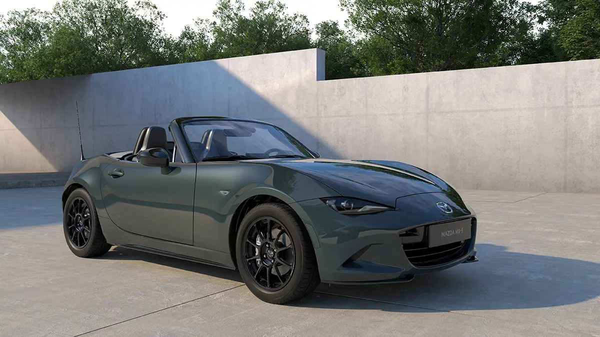 Ein offener Mazda MX-5 Roadster des Modelljahrs 2027 mit der neuen, dunkelgrünen Metallic-Lackierung „Zinc Green“ und schwarzen Leichtmetallfelgen parkiert in einem minimalistischen Studio vor einer grauen Betonwand.