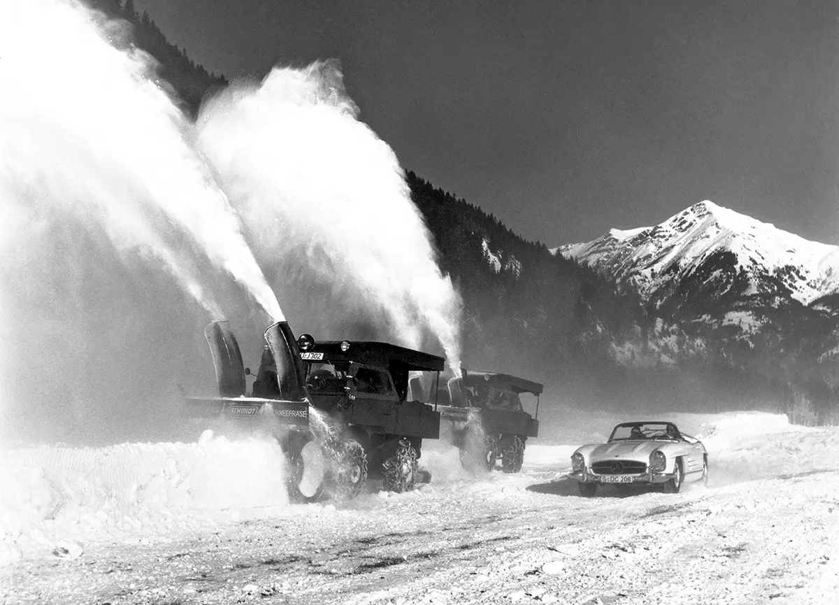 Historisches Archivbild mit zwei Unimog 411 Schneefräsen auf einer Passstrasse und einem Mercedes-Benz 300 SL Roadster im Vordergrund.