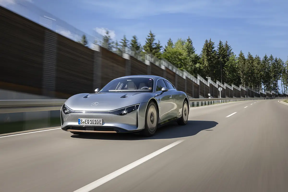 Der silberne Technologieträger Mercedes Vision EQXX fährt auf einer Landstrasse an einer Schutzwand vorbei.