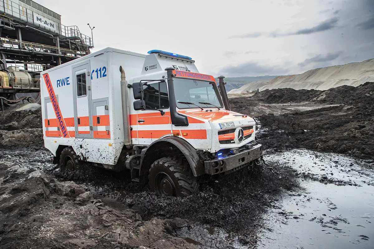 Rot-weisser Unimog Rettungswagen des Rettungsdienstes erkämpft sich seinen Weg durch tiefen Schlamm und Wasserlöcher.