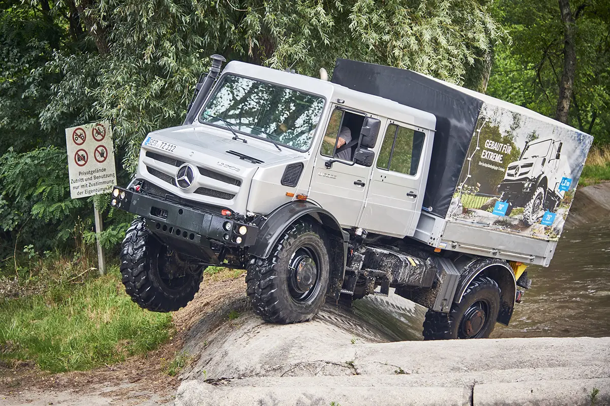Silberner hochgeländegängiger Mercedes-Benz Unimog demonstriert seine extreme Achsverschränkung auf einem Fels-Hindernis.