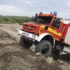 Rot-gelber Unimog Feuerwehrwagen mit Allradantrieb fährt durch schlammiges Gelände bei einer Katastrophenschutz-Übung.