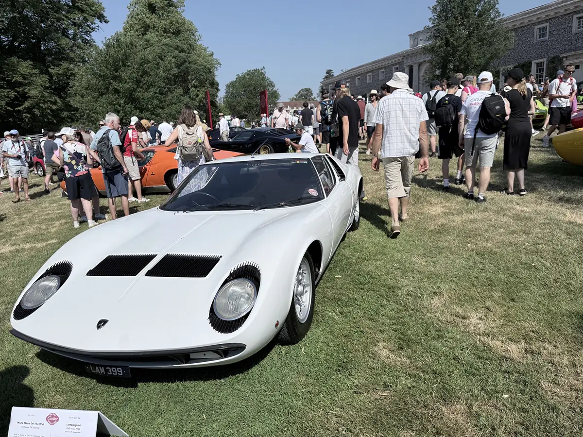 Ein seltener, klassischer Lamborghini Miura in elegantem Weiß parkt inmitten von motorsportbegeisterten Zuschauern auf der Rasenfläche in Goodwood.