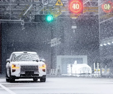 Ein weisser Fahrzeug-Prototyp absolviert Schlechtwetter-Fahrtests in der wetterkontrollierten Testhalle des Geely ECRI Zentrums mit künstlichem Schneefall.