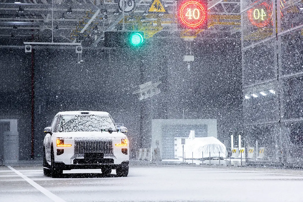 Ein weisser Fahrzeug-Prototyp absolviert Schlechtwetter-Fahrtests in der wetterkontrollierten Testhalle des Geely ECRI Zentrums mit künstlichem Schneefall.