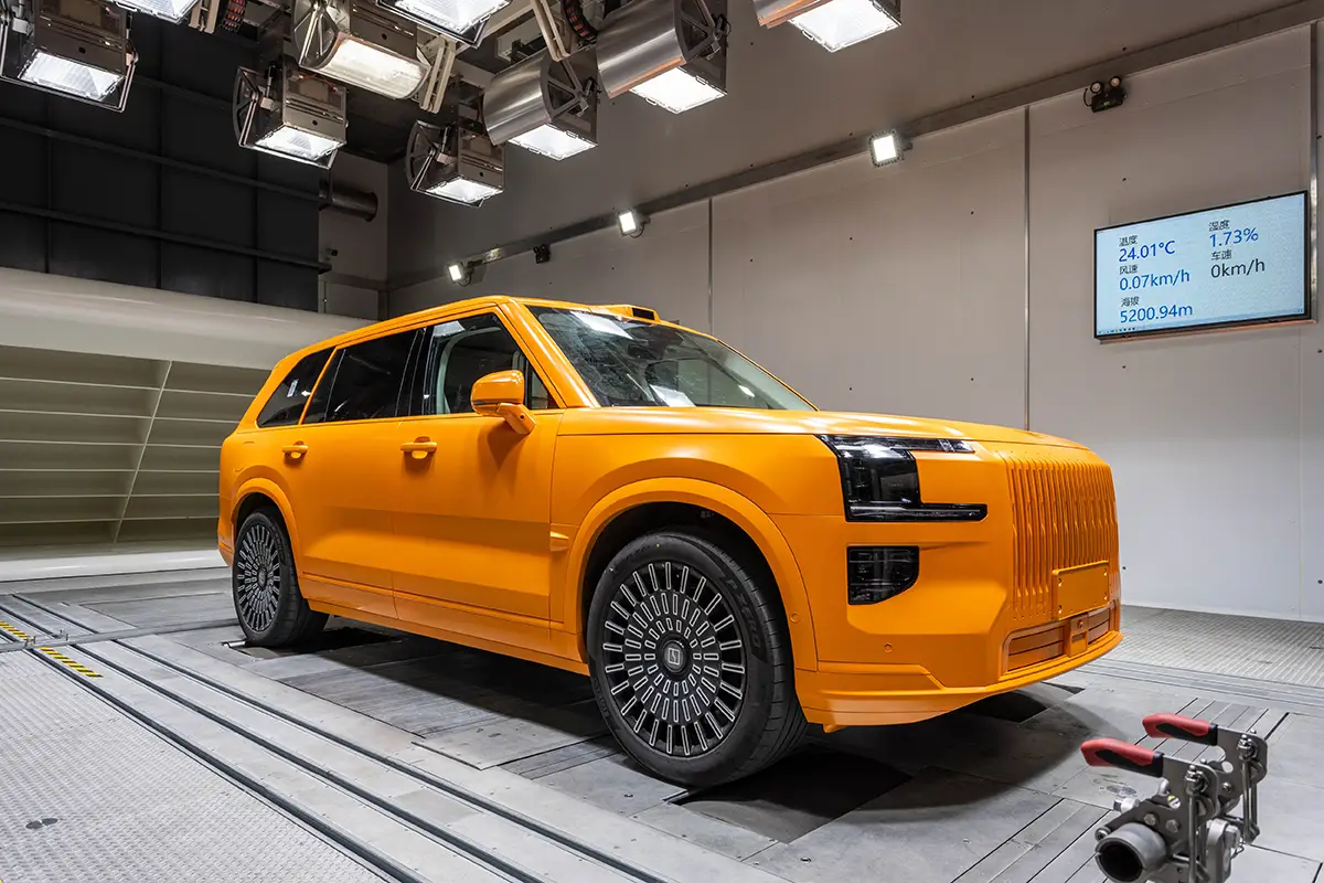 Seitenansicht eines orangen SUVs im High-Tech-Windkanal von Geely unter intensiver Deckenbeleuchtung.