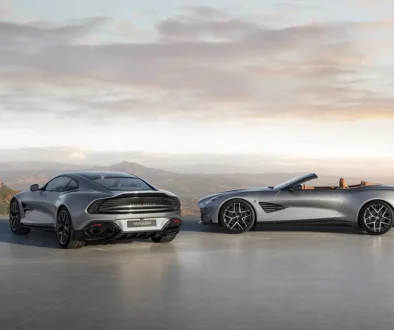 Ein silbernes Aston Martin Vanquish 25 Coupé von hinten und ein offener Vanquish 25 Volante von der Seite auf einem Aussichtspunkt.