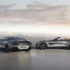 Ein silbernes Aston Martin Vanquish 25 Coupé von hinten und ein offener Vanquish 25 Volante von der Seite auf einem Aussichtspunkt.