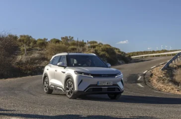 Ein silberner BYD Atto 2, ein kompaktes vollelektrisches Crossover-SUV aus chinesischer Produktion, fährt dynamisch auf einer asphaltierten Landstrasse im hellen Tageslicht.