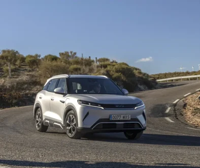 Ein silberner BYD Atto 2, ein kompaktes vollelektrisches Crossover-SUV aus chinesischer Produktion, fährt dynamisch auf einer asphaltierten Landstrasse im hellen Tageslicht.