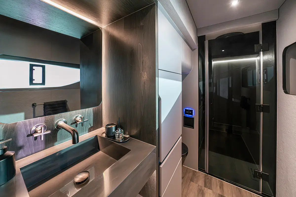 Modernes Badezimmer an Bord der BRABUS ULTIMA 55 mit Edelstahl-Waschbecken, dunkler Holzverkleidung und verglaster Dusche. Foto: Brabus