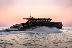 Black luxury speedboat cruising at sunset, creating white spray on calm water with a pink-orange sky.