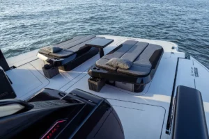 BRABUS Ultima 55: Zwei gepolsterte Sonnenliegen auf dem Deck einer weißen Yacht, dazwischen ein kleiner Tisch, mit Blick auf das blaue Wasser. Foto: Brabus Twin padded sun loungers on a white yacht deck with a small table between, overlooking blue water.