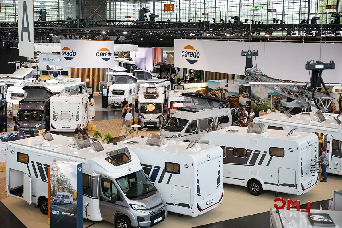 Blick von oben auf die Ausstellungsfläche des Caravan-Salons Düsseldorf mit mehreren modernen, weissen Reisemobilen, integrierten Wohnmobilen und Camper-Vans im Hallenbereich.