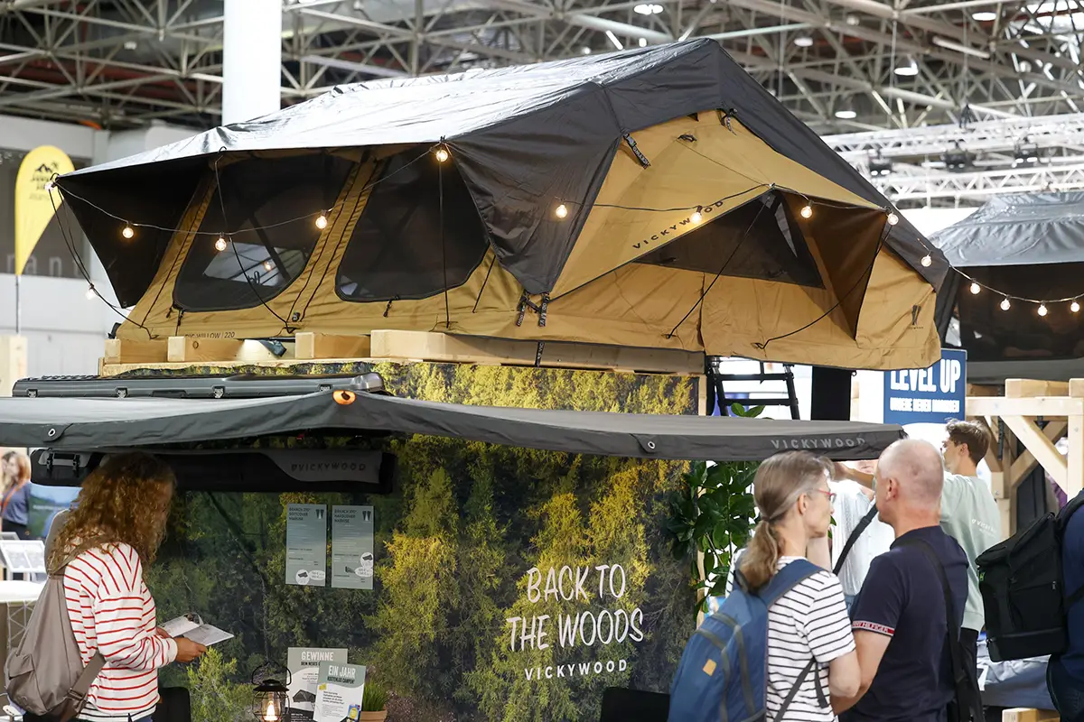 Ein auf einem naturnah gestalteten Ausstellungsstand präsentiertes, braun-schwarzes Dachzelt mit stimmungsvoller LED-Beleuchtung auf dem Caravan-Salon Düsseldorf.