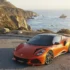 Ein orangefarbener Lotus Emira 420 Sport Mittelmotor-Sportwagen parkiert auf einem Aussichtspunkt an einer Küstenstrasse vor dem Ozean.