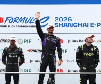 Der Formel-E-Rennfahrer Pascal Wehrlein im schwarzen Porsche-Rennanzug mit lila Helm und verspiegeltem Visier zeigt nach seinem Sieg beim Shanghai E-Prix 2026 triumphierend mit dem Zeigefinger die Nummer Eins.