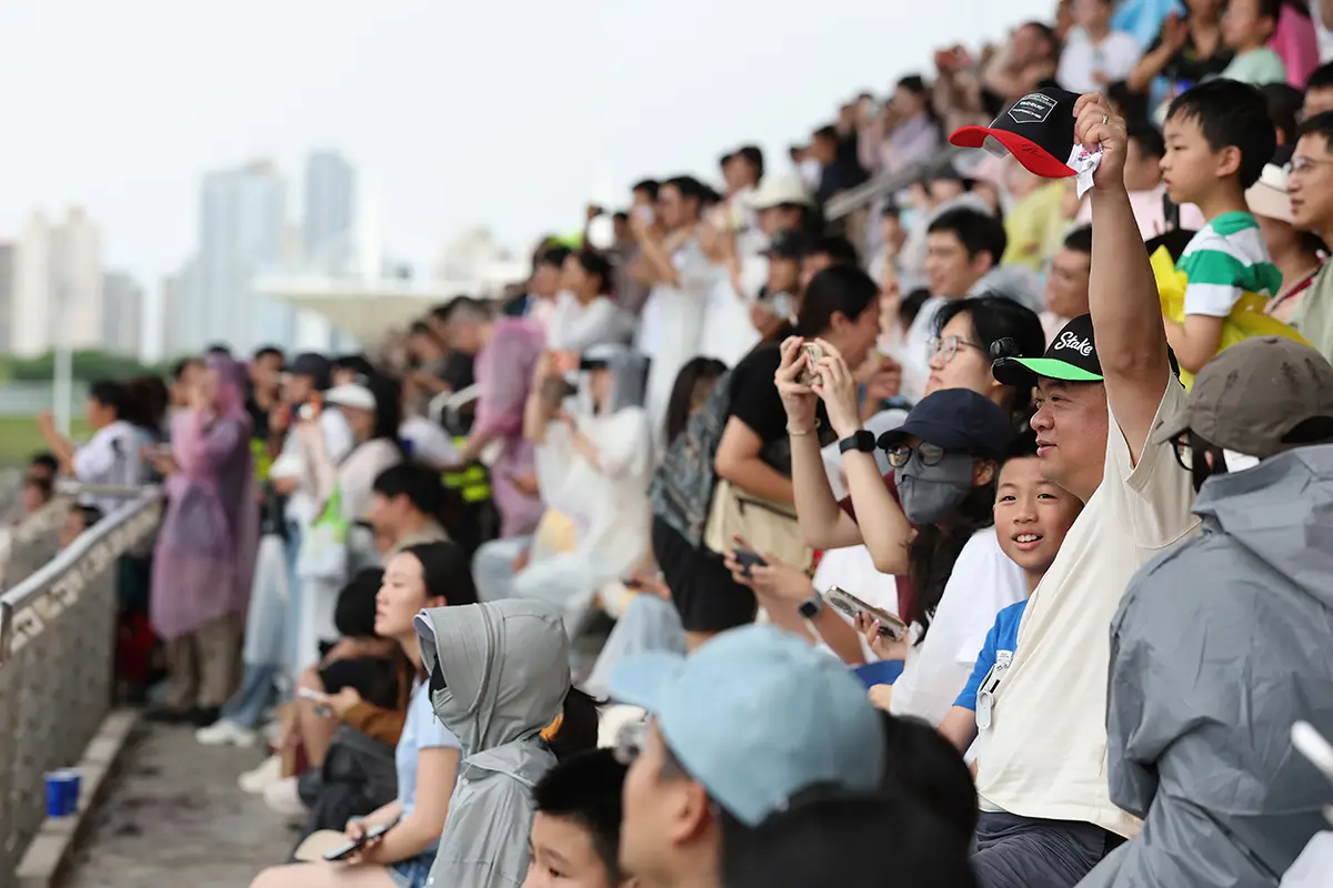 Zuschauertribüne auf dem Shanghai International Circuit voller asiatischer Motorsport-Fans beim Formel E E-Prix 2026, die das Geschehen in der Boxengasse verfolgen und Smartphones für Fotos hochhalten.