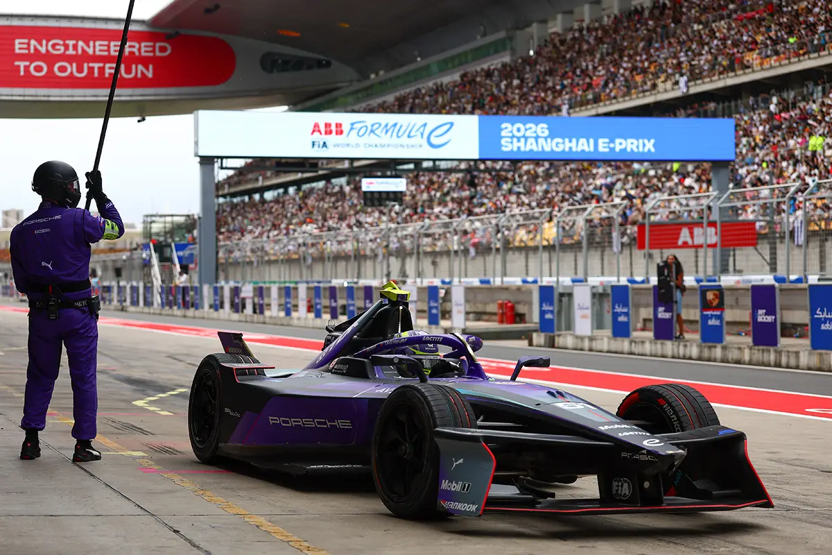 Ein violetter Porsche Formel-E-Rennwagen beschleunigt aus der Boxengasse heraus auf die Rennstrecke in Shanghai, während ein Streckenposten im lila Overall eine Signalleuchte hält.
