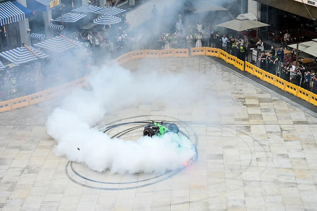 Ein grüner Formel-E-Rennwagen von Envision Racing driftet im spektakulären Showrun im Xintiandi-Viertel von Shanghai und erzeugt dichte, weisse Reifenrauch-Spuren auf dem hellen Asphalt.