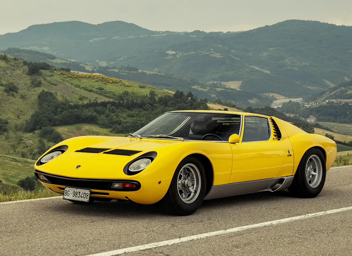 Dreiviertel-Frontansicht des gelben Lamborghini Miura, der am Strassenrand einer Passstrasse in den italienischen Bergen parkt.