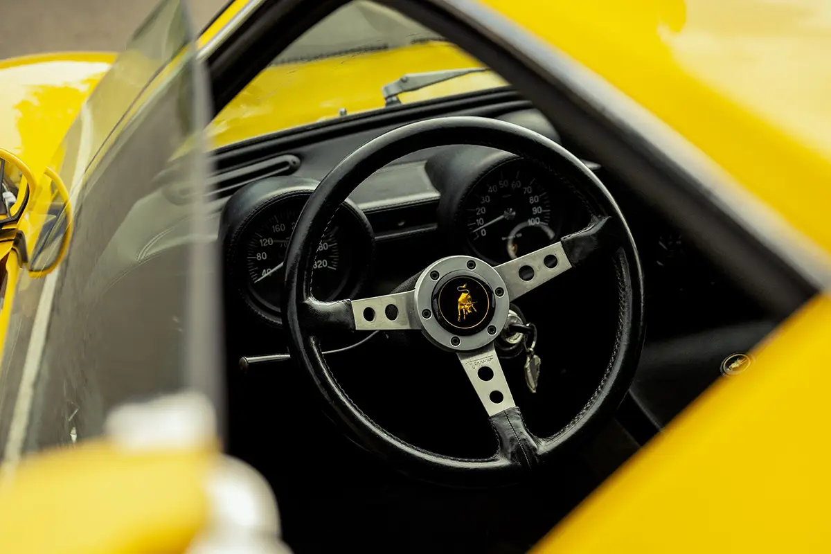 Nahaufnahme des spindeldürren Dreispeichen-Lenkrads mit dem klassischen Lamborghini-Stier-Logo in der Mitte des Miura-Cockpits.