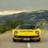 Frontalansicht eines klassischen gelben Lamborghini Miura Supersportwagens auf einer asphaltierten Landstrasse vor einer hügeligen Landschaft.