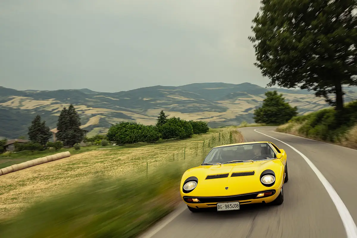Frontalansicht des flachen gelben Lamborghini Miura Supersportwagens in Fahrt auf einer Bergstrasse.