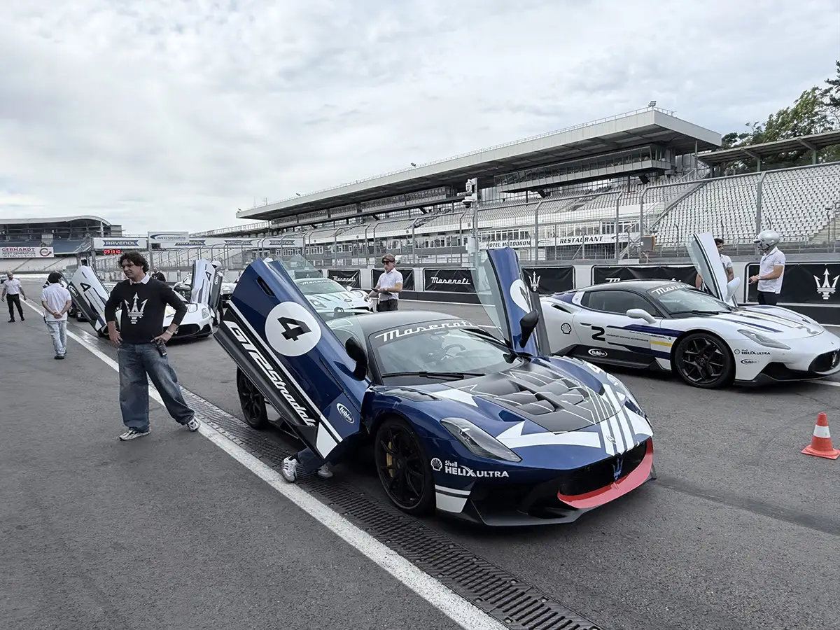Zwei exklusive Maserati Rennsportwagen, darunter ein dunkelblauer GT2 Stradale mit nach oben geöffneten Flügeltüren, stehen in der Hockenheimring-Boxengasse beim ersten Master Maserati Auslandstraining.